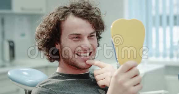 牙科医生在口腔卫生后在牙科诊所的镜子前看着微笑的年轻病人视频的预览图