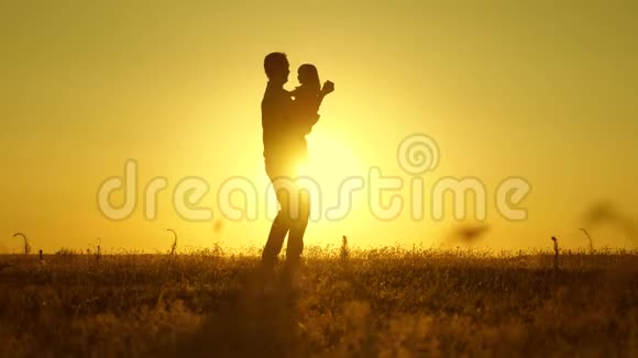 父亲和小女儿在夕阳下翩翩起舞爸爸抱着一个孩子在阳光下的田野里跳舞幸福的视频的预览图