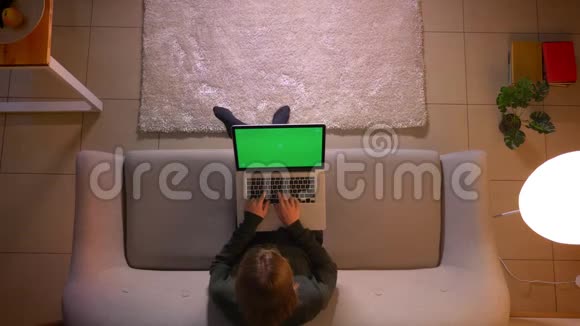 年轻漂亮的女性在笔记本电脑上用绿色屏幕打字的特写镜头坐在室内的沙发上视频的预览图