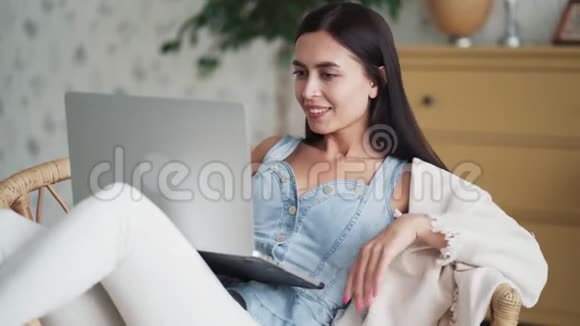 漂亮的年轻女人坐在扶手椅上用笔记本电脑自由职业者在家工作视频的预览图