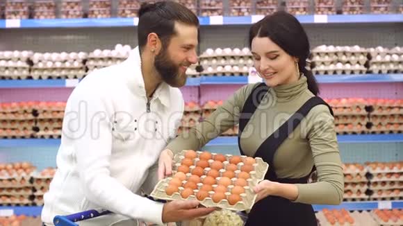 一对幸福的年轻夫妇在超市里拿着一盒鸡蛋的肖像视频的预览图