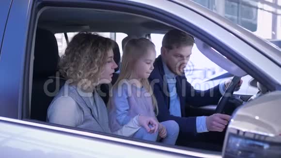 汽车销售中心的幸福客户微笑的家人和孩子一起检查新车同时伸出积极的手势视频的预览图