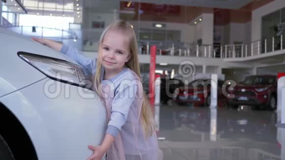 爱汽车快乐的微笑女孩拥抱汽车前照灯在汽车陈列室视频的预览图
