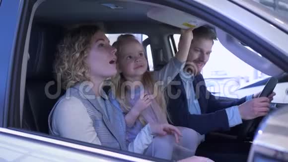 家庭接送购买年轻顾客家庭带着女孩子仔细考虑汽车内饰坐在沙龙内视频的预览图