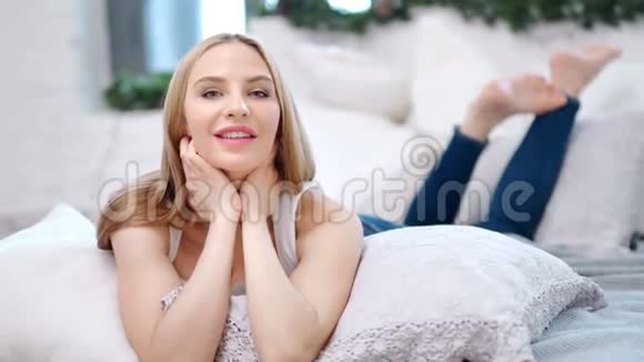 快乐的赤脚迷人的女人躺在舒适的白色室内沙发享受周末视频的预览图