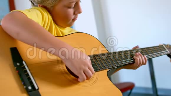 一个金发白种人的小学生坐在书桌前在教室里弹吉他视频的预览图