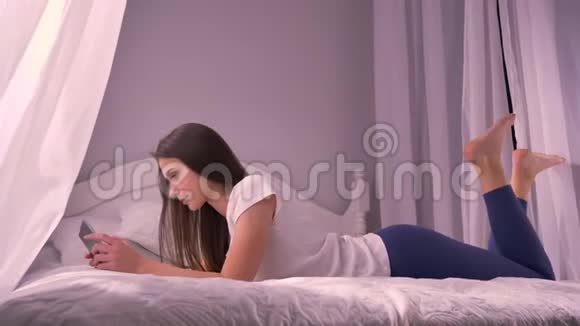 在平板电脑上随意躺在家里的床上的年轻白种人女性特写照片视频的预览图