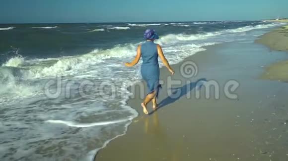 年轻漂亮的女人沿着海滨跑她高兴沙滩和海浪慢动作女人微笑这就是视频的预览图