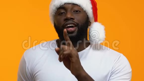 戴着节日礼帽的长胡子黑公男做着沉默的手势展示着礼物盒视频的预览图
