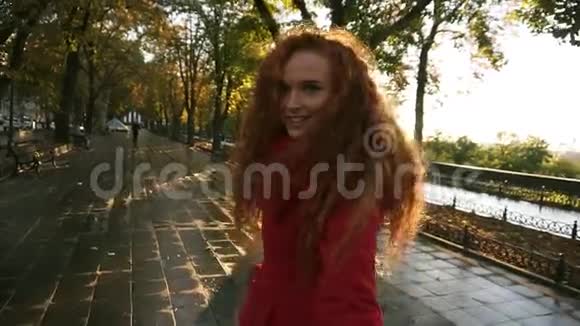 年轻的白种人女人在潮湿的小巷旁的一个五彩缤纷的秋天公园里散步欣赏秋天的树叶快乐地转过身视频的预览图