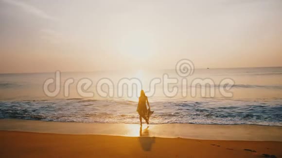 史诗般的剪影拍摄的年轻快乐的女人看着令人惊叹的日落田园般的金色海洋海滩与银波视频的预览图