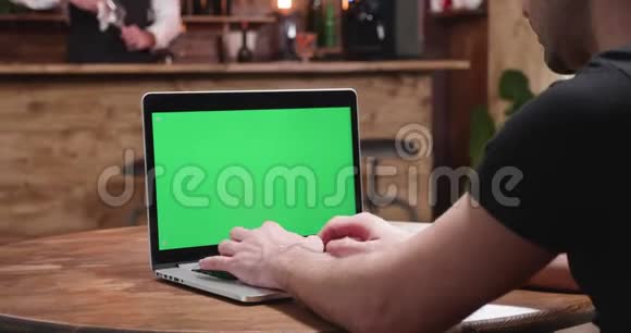 一个穿着休闲紧身衣的年轻人在带绿色屏幕的笔记本屏幕视频的预览图
