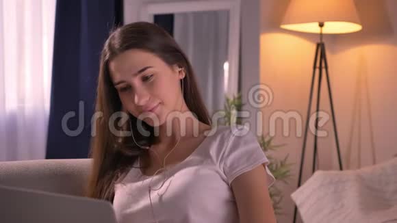 年轻迷人的少女在手机上浏览时用耳机听音乐的特写镜头视频的预览图