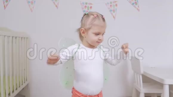 小女孩带着玩具蝴蝶翅膀挥舞着她的手臂在后面在托儿所跳舞视频的预览图