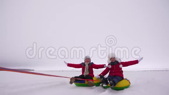 快乐的女孩在冬天的雪地里雪橇挥舞着双手孩子们在充气的雪管上滑动大笑和视频的预览图