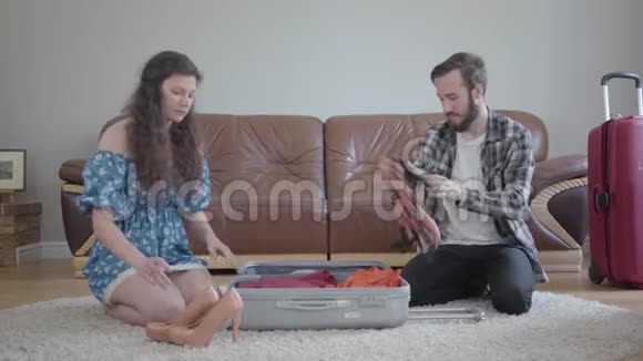 肖像男女坐在地板上在家里的一个皮革沙发前面旅行前收拾一个手提箱这就是视频的预览图