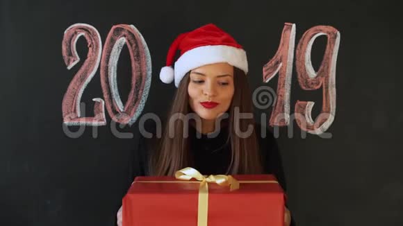 年轻女子在圣诞老人的帽子上的石板墙背景与铭文2019年女孩微笑着她会很高兴视频的预览图