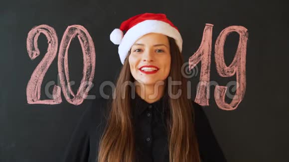 一个戴着圣诞老人帽子戴着黑色石板墙的快乐女孩的肖像新年快乐视频的预览图