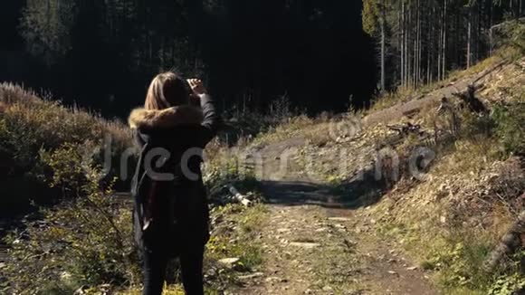 年轻女孩徒步旅行者正在用手机摄像头拍摄美丽的森林景观视频视频的预览图
