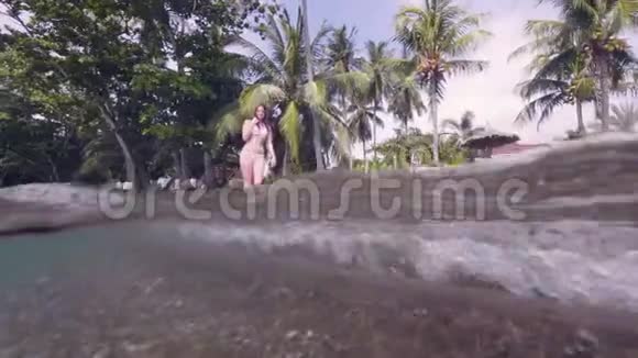 迷人的女人穿着比基尼在棕榈树背景下的海水海滩上散步水线观看泳装美女视频的预览图