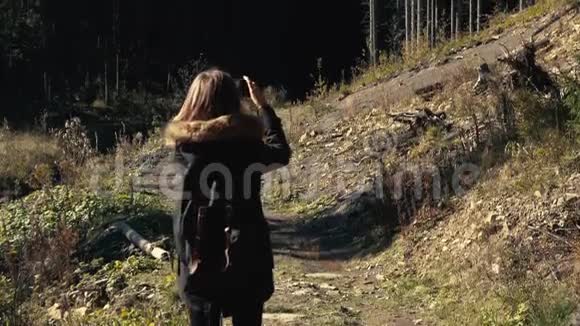 年轻女孩徒步旅行者正在用手机摄像头拍摄美丽的森林景观视频视频的预览图