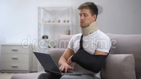 戴泡沫颈项圈和手臂吊带的受伤男子在笔记本电脑上工作时感到疼痛视频的预览图