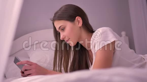 年轻活泼的白种人女性的特写镜头她使用平板电脑躺在床上大笑然后看着视频的预览图