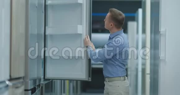 这个人打开电器商店冰箱的门与其他型号的人比较来买新房子视频的预览图
