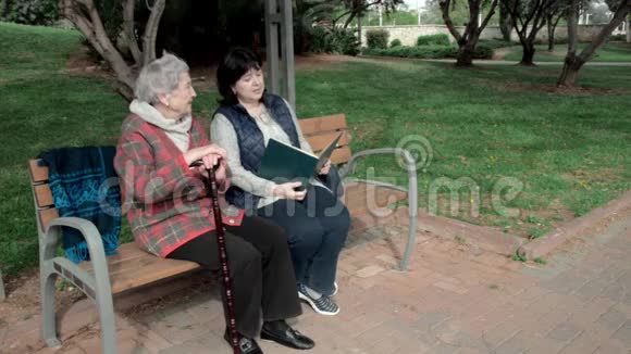 志愿者为坐在城市公园长凳上的老年妇女阅读书籍视频的预览图