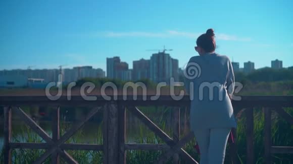 一个年轻的女孩站在湖岸上背景是城市景观和蓝天视频的预览图