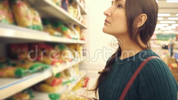 穿绿色毛衣的布鲁内特女士选择超市里的面食视频的预览图