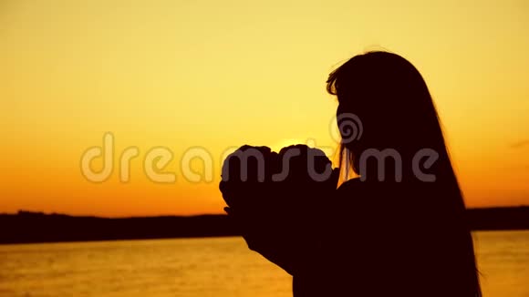 悲伤的女孩在金色的太阳落山时捧着她的心视频的预览图