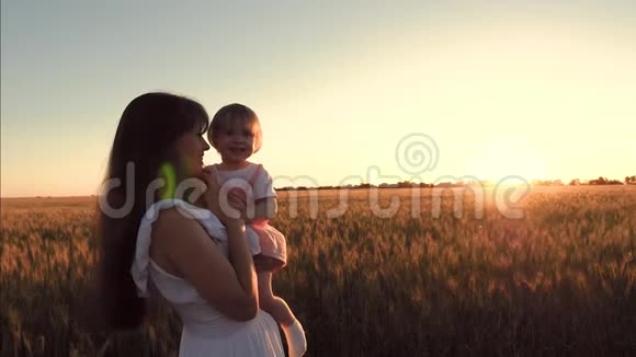 快乐的妈妈把她的小女儿抱在怀里抱在美丽的夕阳下的一片麦田上幸福家庭视频的预览图