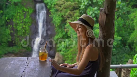 一位年轻女子在一家美丽的咖啡馆里慢镜头在峡谷和瀑布上欣赏着壮丽的景色视频的预览图