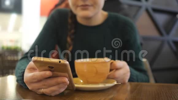 穿着绿色毛衣手里拿着手机喝饮料的不可辨认的女性视频的预览图
