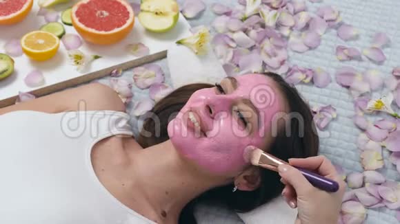可爱的白种人女人在健康中心放松的肖像而美容师使用化妆刷敷粉红色面具视频的预览图