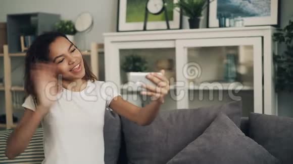 微笑着年轻的非洲裔美国妇女正在做在线视频电话看着智能手机屏幕谈笑风生视频的预览图