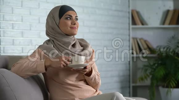爱做梦的女士坐在沙发上喝杯茶享受休闲时光回家视频的预览图