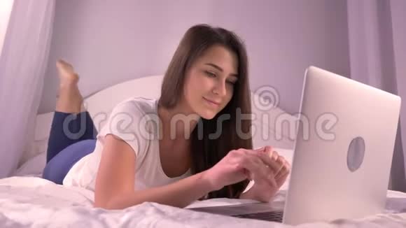年轻漂亮的少女躺在床上发短信微笑的特写照片视频的预览图