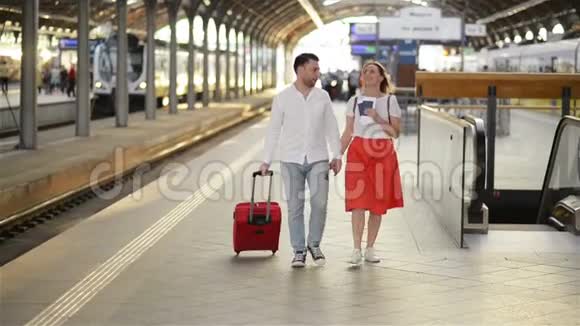 白种人有吸引力的妻子和丈夫在火车站散步带着手提箱在车轮上一边说话视频的预览图