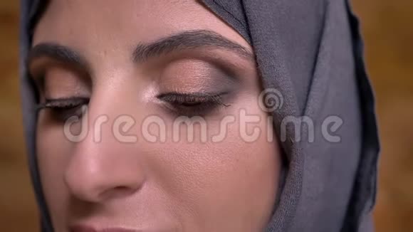 戴着头巾的中年穆斯林妇女的特写镜头在布里克肯墙上用明亮的化妆观看视频的预览图