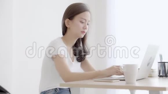漂亮的年轻自由职业亚洲女性微笑着工作着笔记本电脑在办公室里用电话交谈顾客女孩用n视频的预览图
