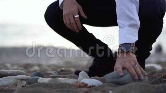 海滩上的人试图用灰色的石头建造金字塔但这并不容易石头掉了下来视频的预览图