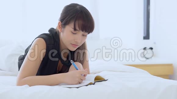 美丽的肖像亚洲女人放松躺在床上思考想法在卧室写书或日记视频的预览图