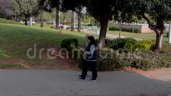 女性照顾者帮助一位老年妇女在城市公园散步视频的预览图