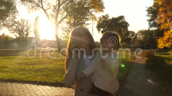 妈妈抱着孩子在智能手机上聊天在日落时分在秋天公园散步快乐的宝宝视频的预览图