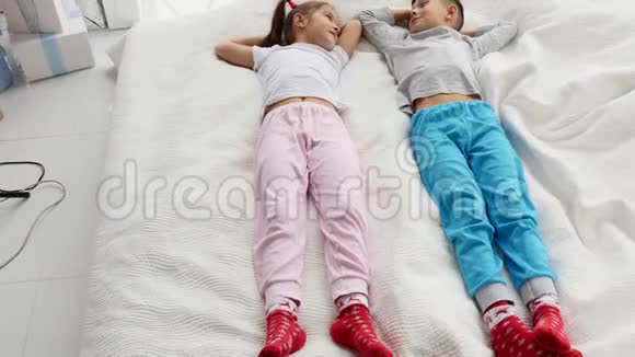 两个可爱的孩子躺在舒适的沙发上双手捂住头准备小睡一会儿视频的预览图