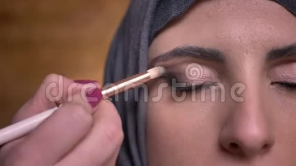 用刷子为穆斯林妇女在布里克肯墙上的头巾做眼妆的女性手的特写半像视频的预览图