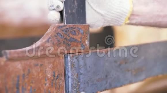 在模糊的木木上在施工现场用防护手套将生锈的金属细节固定在人手上视频的预览图