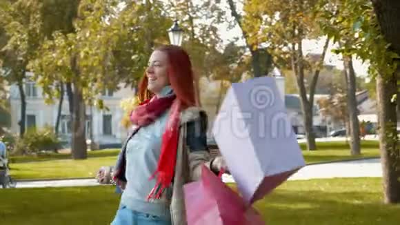 快乐的女孩带着狐臭的头发在公园里散步用多种颜色的纸袋购买并感到高兴视频的预览图